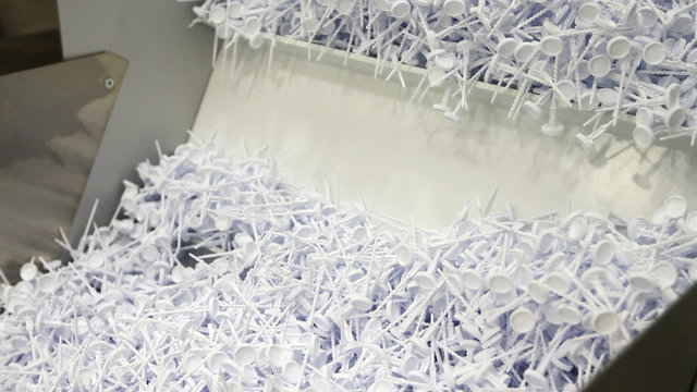 Small plastic parts being scooped onto a conveyor system in a factory
