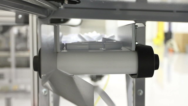 Tilting down from a conveyor belt carrying small plastic parts and dropping them into a bin in a factory.
