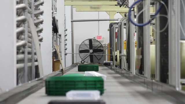 Time lapse, looking down a conveyor belt in a factory as robotic arms deliver plastic products onto the belt. 
