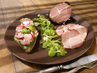 Crude, dried gammon ham with sandwich, salad on plate on wooden board