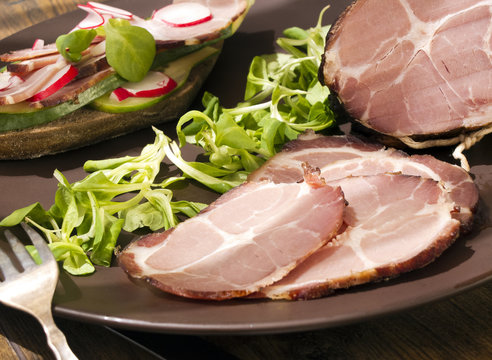 Crude, dried gammon ham with sandwich, salad on plate on wooden board