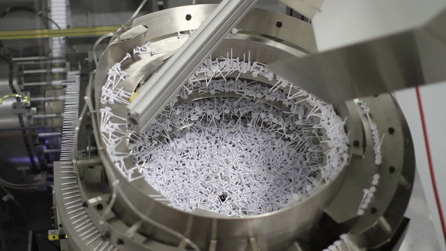Tilting down, showing a large piece of machinery assembling plastic parts into a chapstick product in a factory
