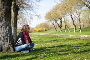 thoughtful brunette sitting under a tree in a park on a sunny da