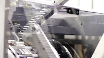 Tilting down, showing a large piece of machinery assembling plastic parts into a chapstick product in a factory
