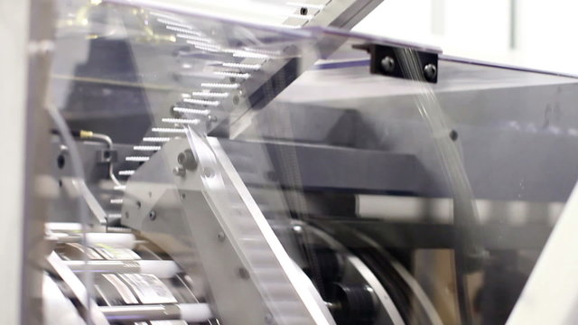 Tilting down, showing a large piece of machinery assembling plastic parts into a chapstick product in a factory
