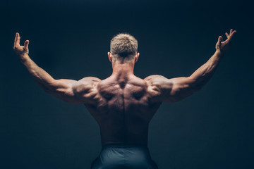 Handsome muscular bodybuilder posing over black background.