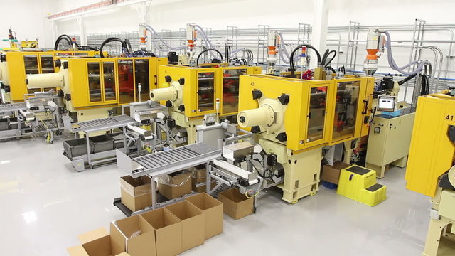 Crane shot in a clean factory, showing multiple large, industrial injection molding machines. 
