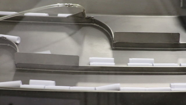 Close-up of small plastic parts (chapstick housing) being sorted as the move through a conveyor system in a factory
