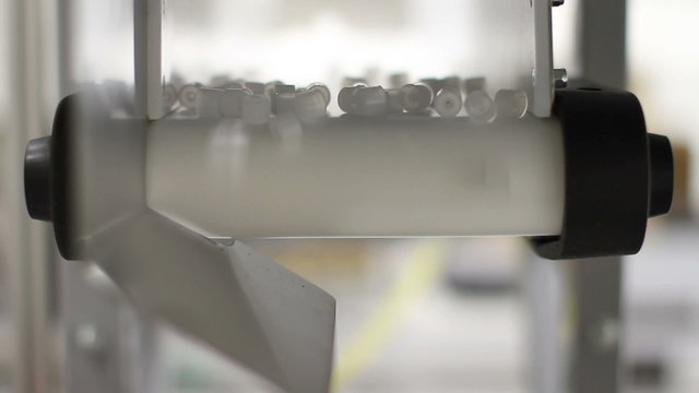 Small plastic parts dropping off a conveyor belt in a factory, with shallow depth of field
