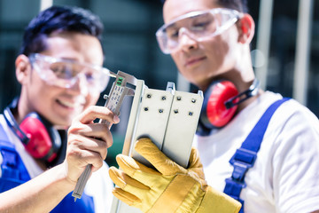 Asian worker checking work piece in production plant