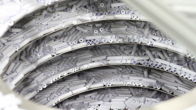 A conveyor system in a factory moves small plastic items (chap stick housing) upward to where they are sorted
