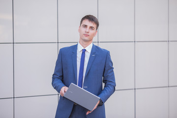 Successful businessman standing in the street holding a laptop