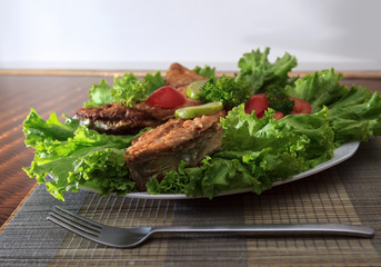 A piece of fried fish fillett served on blue glass table with lettuce, lime, tomato and herbs