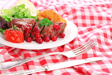 Tasty roasted meat with cranberry sauce and roasted vegetables on plate, on color wooden background