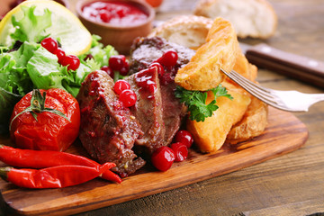 Beef with cranberry sauce, roasted potato slices on cutting board, on wooden background