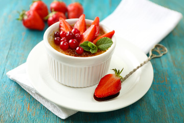 Creme brulee dessert with fresh strawberries and mint leaves, on color wooden background