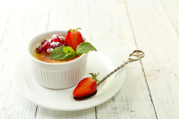 Creme brulee dessert with fresh strawberries and mint leaves, on color wooden background