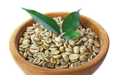 Green coffee beans with leaves in bowl close up