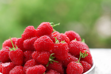 Fresh raspberries in bowl on blurred nature background
