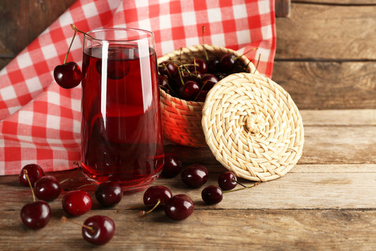 Glass of cherry juice on wooden table with checkered napkin on background