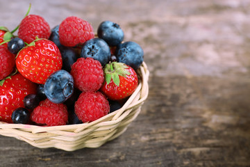 Sweet tasty berries in basket on wooden table close up