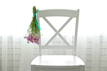 Bouquet of wild flowers drying on chair on light background