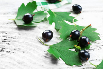 Ripe black currants with green leaves on wooden table, closeup