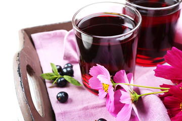 Glasses of fresh blackcurrant juice on wooden tray with pink napkin and flowers, closeup