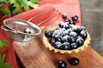 Delicious crispy tart with black currants on wooden cutting board, closeup