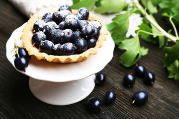 Delicious crispy tart with black currants on white stand on wooden table, closeup