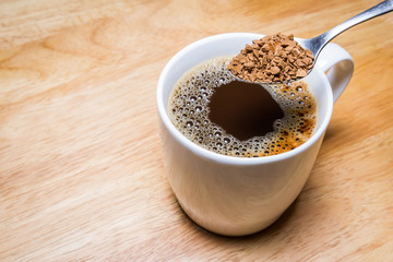 Cup of coffee and spoon of Coffee Granules on wooden table. focus on Granules.