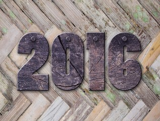 The word "2016" written in rusty metal letterpress type sitting on a wooden ledge background.