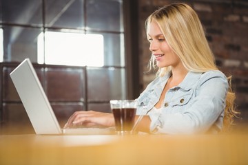 Smiling blonde having coffee and using laptop