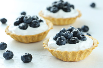 Dessert tartlets with blueberries on white wooden background