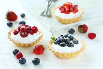 Dessert tartlets with berries on white wooden background