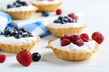 Dessert tartlets with berries on white wooden background