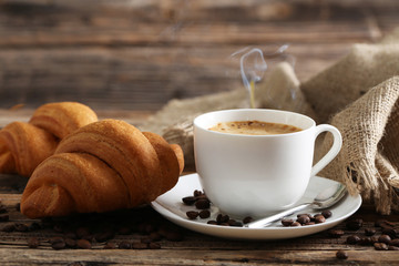 Delicious croissants with cup of coffee on brown wooden backgrou