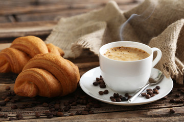 Delicious croissants with cup of coffee on brown wooden backgrou