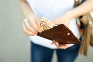 Girl is taking out fifty-euro banknote from her leather wallet