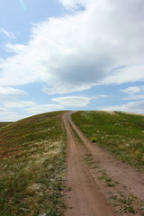 Fototapeta na wymiar Steppe dirt road towards a hill top against a blue sky