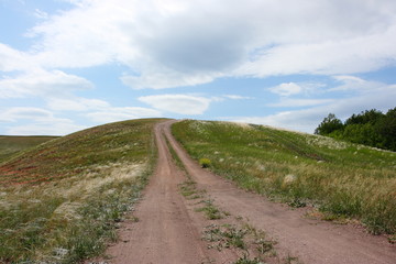 Fototapeta na wymiar Steppe dirt road towards a hill top against a blue sky