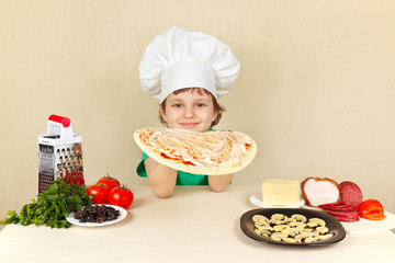 Little boy in chefs hat smeared with sauce on the pizza crust