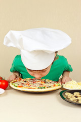 Little funny chef sniffing the aroma of cooked pizza