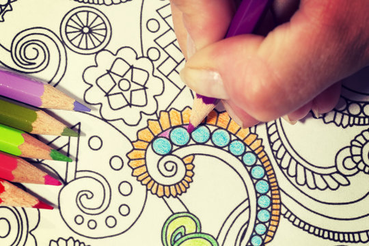 An image of a new trendy thing called adults coloring book.  In this image a person is coloring an illustrative and detailed pattern for stress relieve . Image has a vintage effect applied.