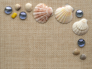 Sea theme background frame with seashells, scallops and blue glass pebbles on the rough weave textile mat.