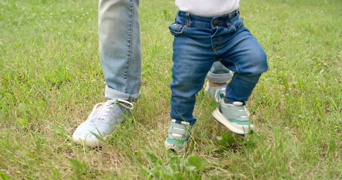 Legs of baby boy walking on grass helped by his father  