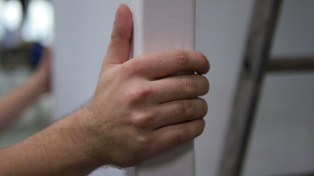 Close up of the hands of a man carrying a white canva in a hall.