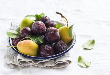 fresh plums and pears on a white enamel plate on a light background