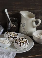 meringue with chocolate sauce and nuts on a white plate on brown wooden surface