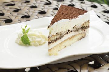 tiramisu cake served with whipped cream in the white dish